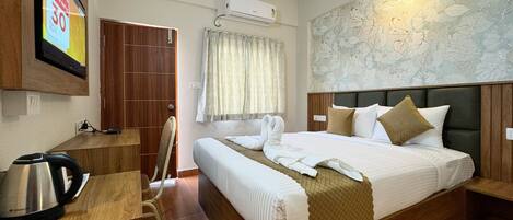A hotel room with a bed, a desk with a kettle, a wardrobe, and a wall-mounted air conditioner.