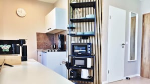 Une cuisine moderne dotée d’un four, d’un micro-ondes et d’une machine à café encastrés, d’un mur avec des lambris en bois et d’une porte blanche.