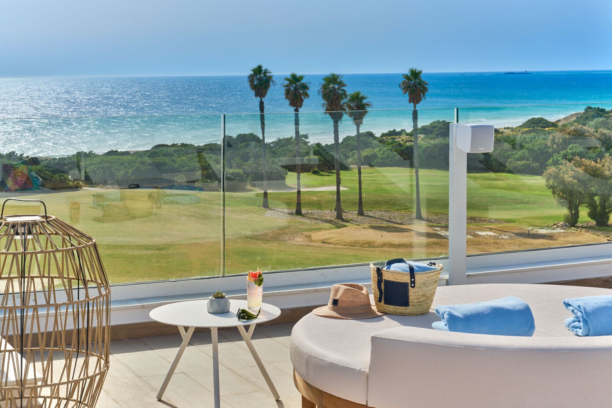 Un balcón con vistas al mar, un campo de golf y un sofá blanco con una toalla azul.