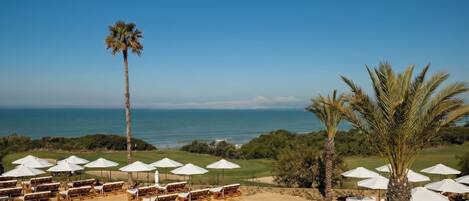 A pool area with checkered tiles, lounge chairs, and umbrellas, overlooking a beach and ocean.