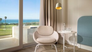 A modern room with a view of the ocean, a beige armchair, a small table with a lamp, and a blue sofa. - Amàre Beach Hotel Sancti Petri - Adults Recommended (Chiclana de la Frontera)