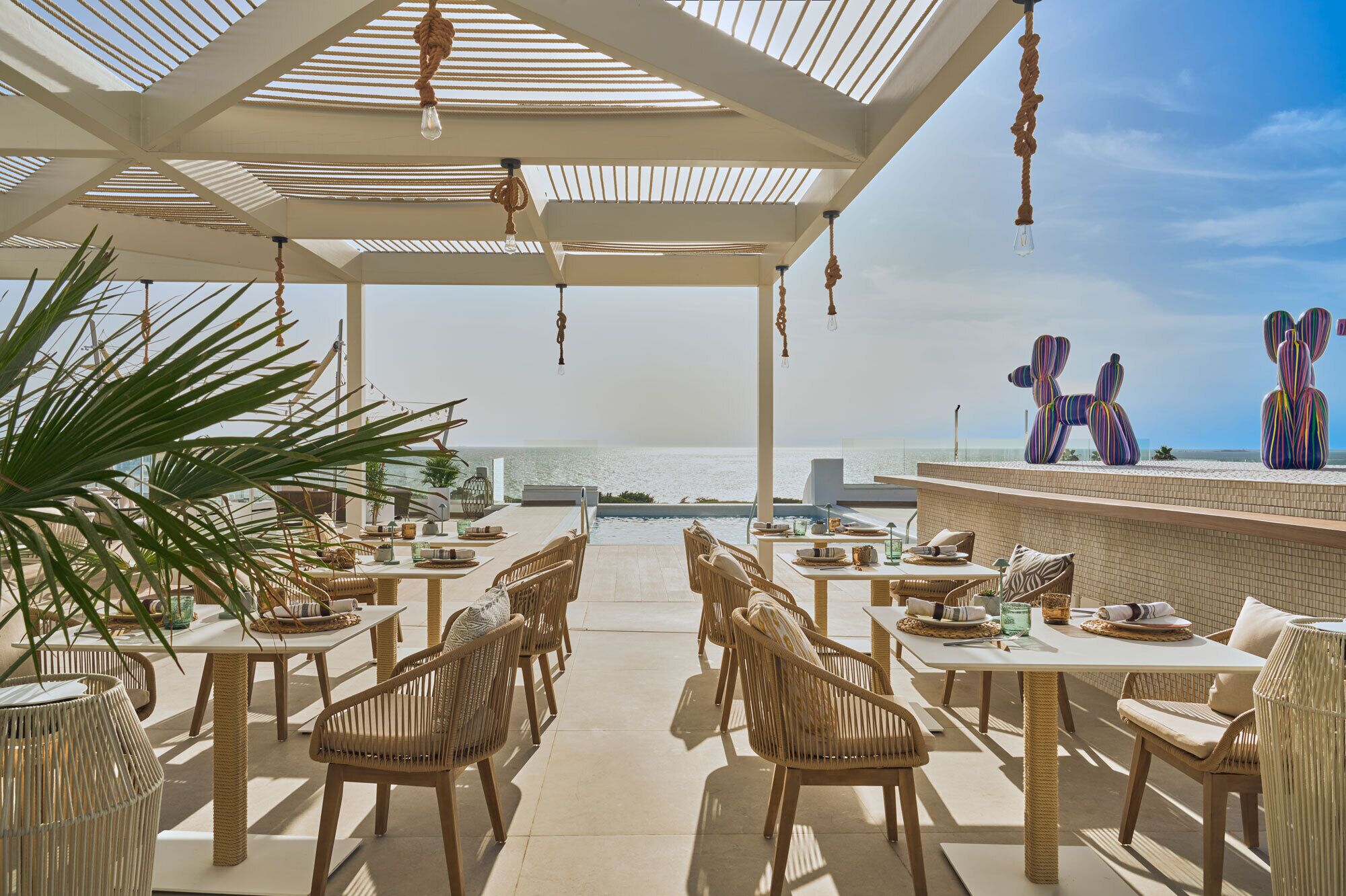 An outdoor dining area with wicker furniture, a pool, and a view of the sea.