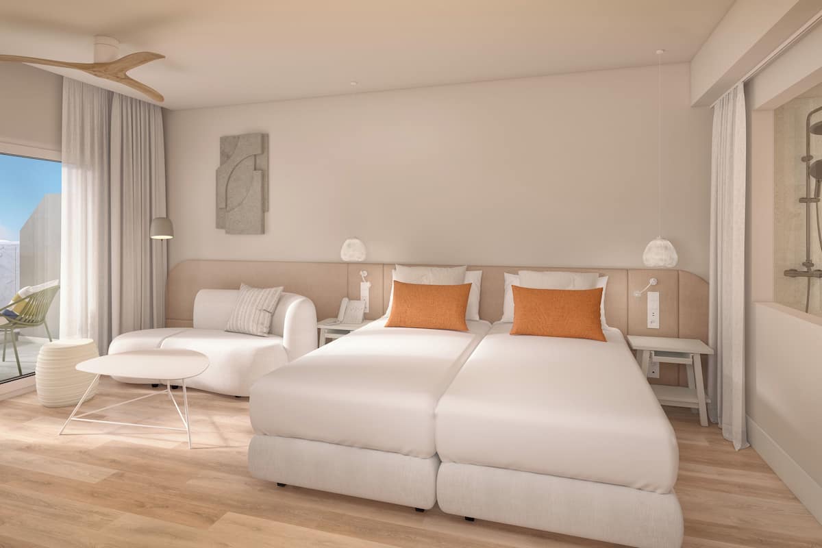 Quarto de hotel moderno com uma cama grande, um sofá, uma mesinha e uma escrivaninha.
