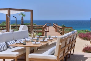 A wooden deck with a dining table set for two, overlooking the ocean.