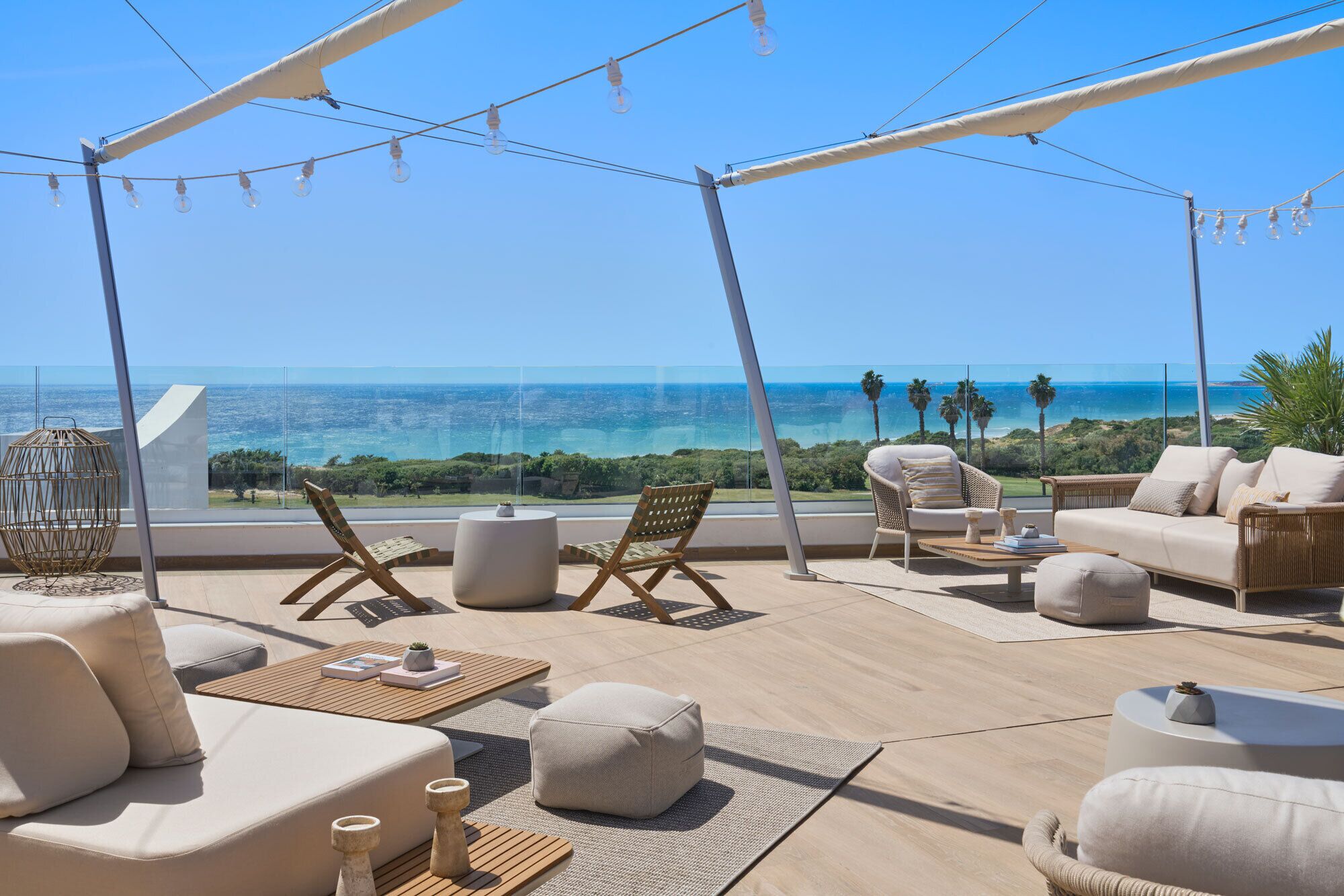 Een zonnig terras in de open lucht met uitzicht op zee, ingericht met banken, stoelen en tafels.