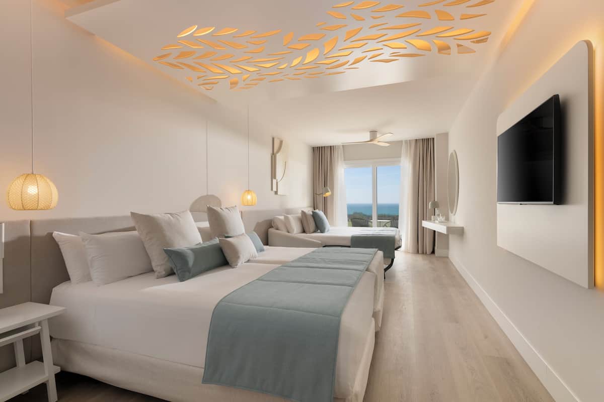 Quarto de hotel moderno com uma cama grande, televisão, luminária de teto e vista para o exterior.