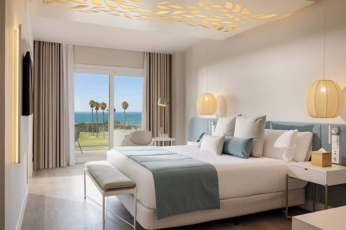 Quarto de hotel moderno com uma cama grande, uma mesa de trabalho e vista para o oceano.