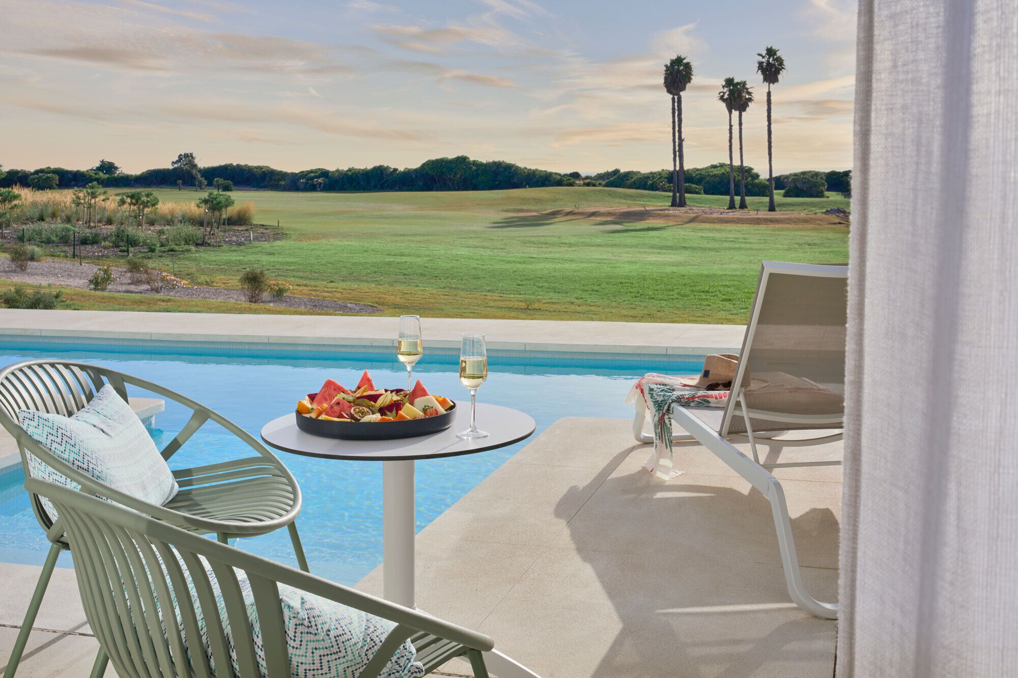 Un cadre agréable au bord de la piscine, avec une table dressée pour deux personnes, une chaise et une vue sur un terrain de golf.