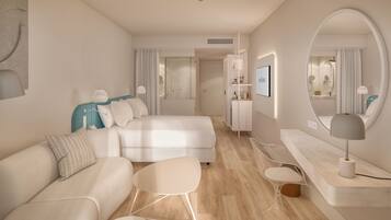 A modern hotel room with a large bed, a sofa, a small table, a chair, and a vanity with a mirror.