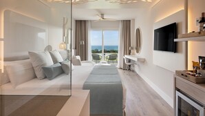 A modern hotel room with a bed, seating area, TV, and a balcony with a view. - Amàre Beach Hotel Sancti Petri - Adults Recommended (Chiclana de la Frontera)