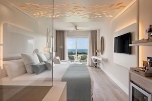 Quarto de hotel moderno com cama, área de estar, TV e varanda com vista.