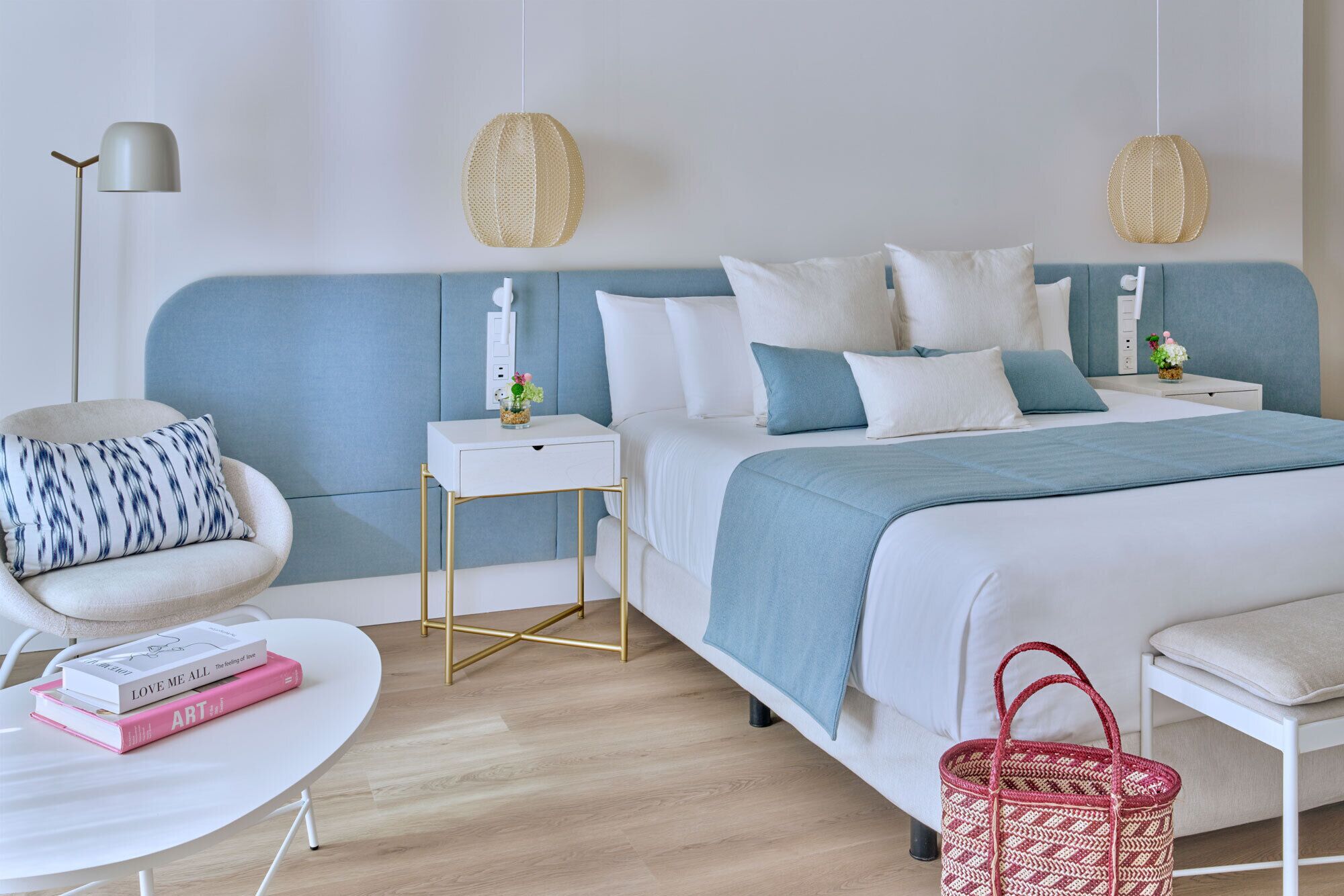 A modern bedroom with a bed, bedside tables, a chair, a small table with books, and a floor lamp.