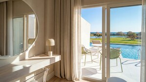 A modern hotel room with a large window, a round mirror, a small table with a lamp, and a view of a swimming pool and landscape. - Amàre Beach Hotel Sancti Petri - Adults Recommended (Chiclana de la Frontera)