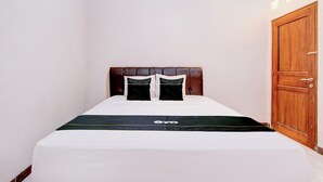 Cama bem arrumada com colcha branca e manta preta, cabeceira de madeira e porta de madeira à direita.