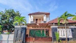 Uma casa de dois andares com telhado de telhas, um portão verde e uma varanda.