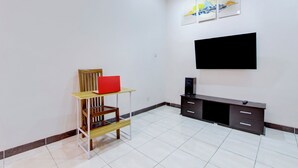 Uma sala de estar moderna com uma televisão de tela plana fixada na parede, um suporte de madeira para TV com um objeto vermelho em cima e piso de azulejos.