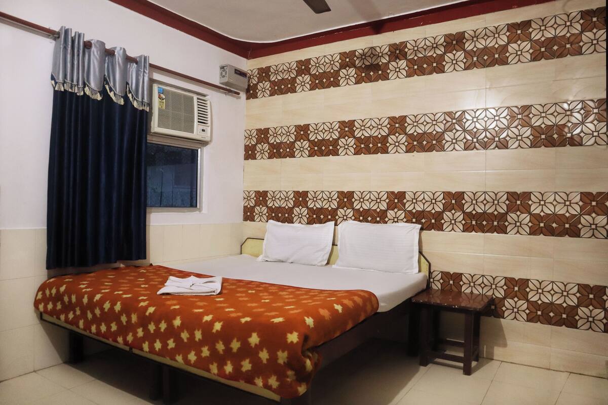 Habitación de hotel con cama, ventana con cortinas, equipo de aire acondicionado y un diseño decorativo en la pared.