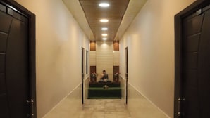 A hallway with a person sitting on a bench, doors on both sides, and a tiled floor. - Laugh Tale Hostel (Rishikesh)