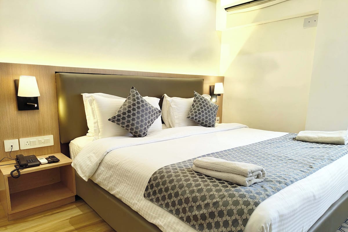 Habitación de hotel con una cama grande, una mesita de noche con teléfono y lámpara, y un equipo de aire acondicionado instalado en la pared.