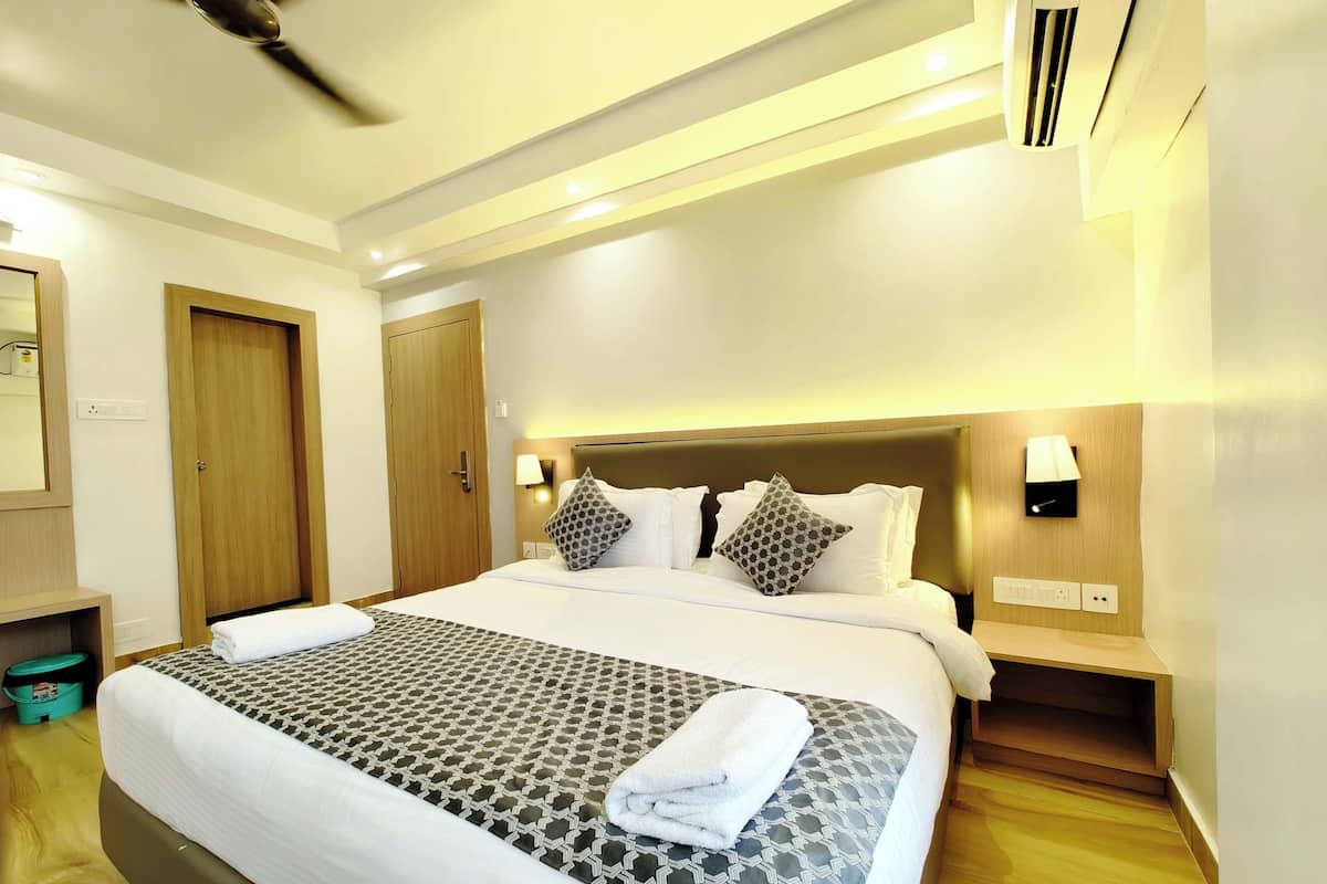 Una habitación de hotel con una cama grande, un ventilador de techo, un aire acondicionado instalado en la pared y una mesita de noche con lámpara.