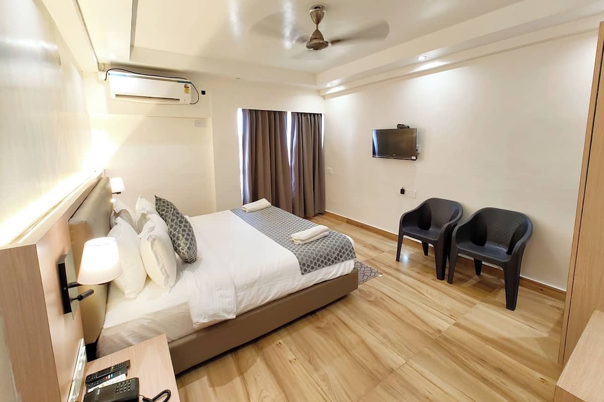 Una habitación de hotel moderna con una cama grande, un ventilador de techo, un televisor y un rincón de descanso con dos sillones.