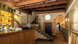 Un comptoir d’accueil en bois, agrémenté d’un présentoir pour vins et spiritueux, d’un escalier et d’une enseigne indiquant « FABBRICA EST. 2006 ».