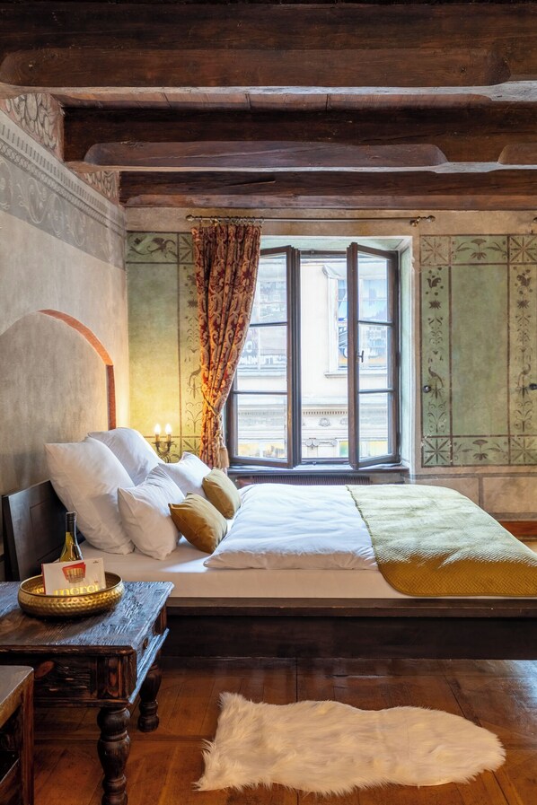 A traditional room with a wooden bed, a nightstand, a fur rug, and a window with curtains.
