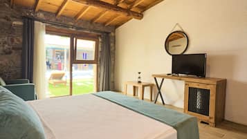 A bedroom with a bed, a television on a wooden cabinet, a small table, and a window with a view of the outside.