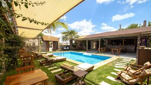 Ein Garten mit Swimmingpool, Holzliegen, Grillplatz und einem Steinhaus.