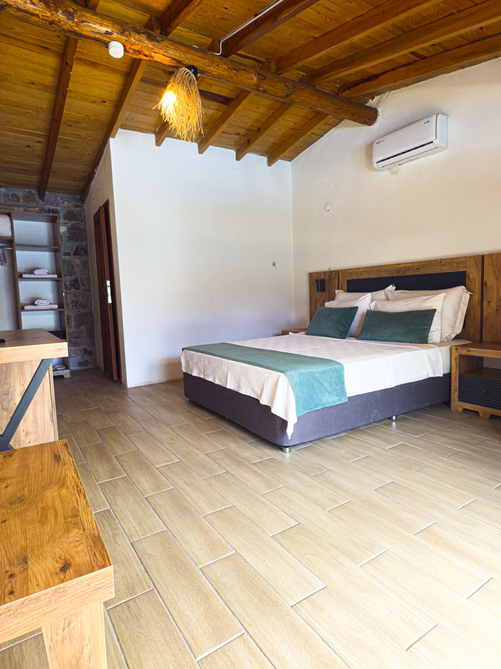 Quarto com cama de madeira, mesa de cabeceira, escrivaninha de madeira e parede de pedra.
