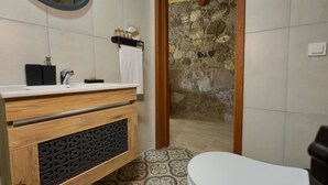 Ein Badezimmer mit einem Holzlagerflächenmöbel, einem Spiegel, einer weißen Toilette und einer Steinwand.