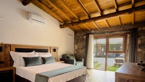 Ein Schlafzimmer mit einem hölzernen Bett, einem Nachttisch, einem Stuhl und Blick ins Freie durch eine Glastür.
