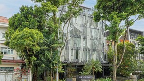 Un edificio moderno con fachada de vidrio, rodeado de exuberante vegetación y un letrero que indica que es un complejo de apartamentos con servicios.