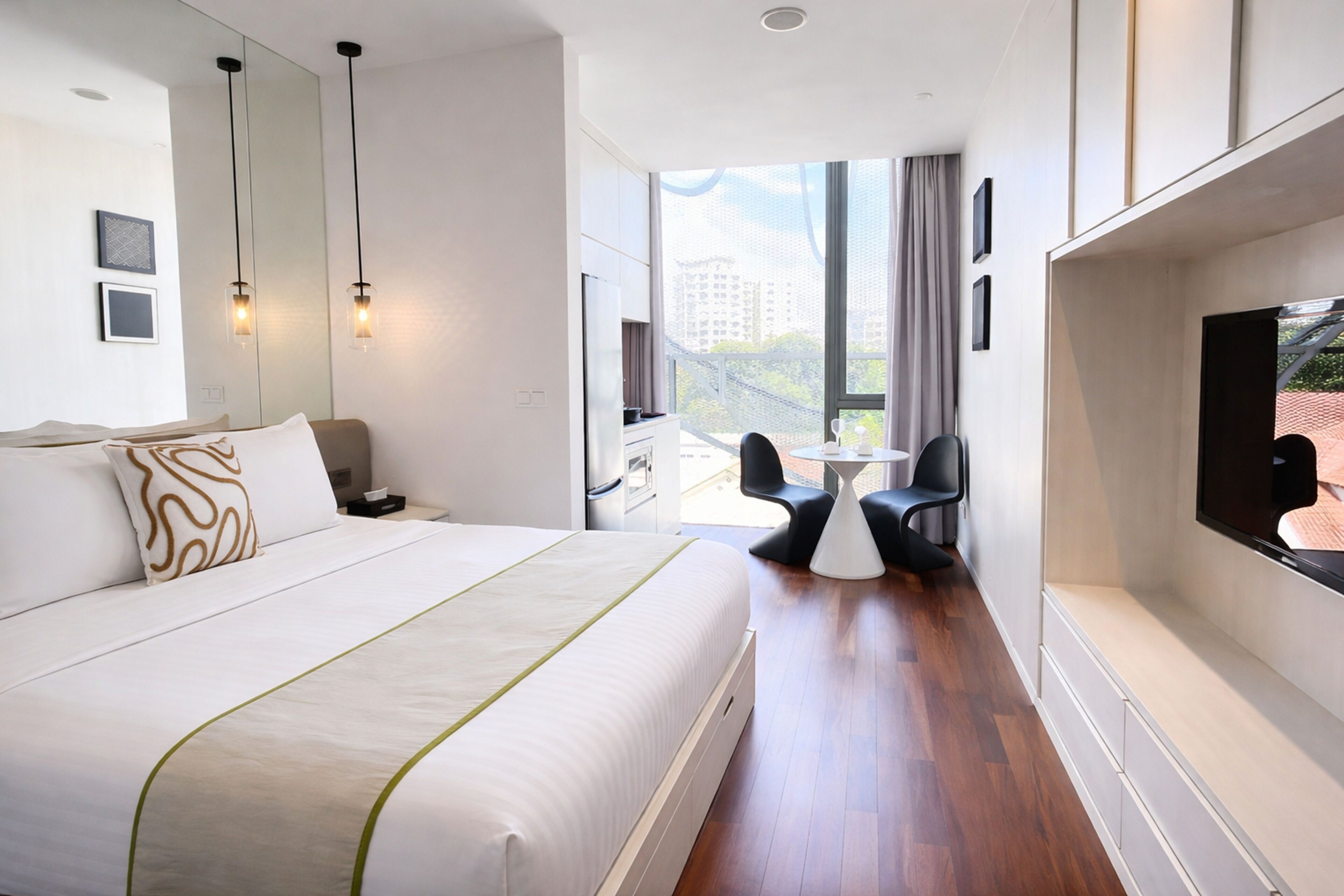 A modern hotel room with a large bed, a desk, a chair, and a TV.