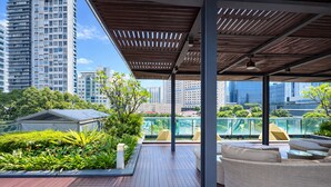 Una terraza en la azotea con mobiliario exterior, una cubierta de madera y vistas a edificios altos.