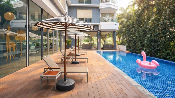 Un área de piscina moderna al aire libre con sillones de descanso y sombrillas, rodeada de paredes de cristal y una terraza de madera.