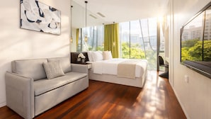 Una habitación de hotel moderna con cama, sofá, un amplio ventanal con vista a la ciudad y un cuadro en la pared.