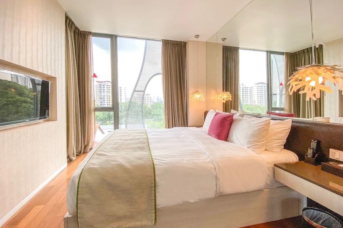 Ein Hotelzimmer mit einem großen Bett, einem Nachttisch, einem Spiegel und Blick auf die Stadt.