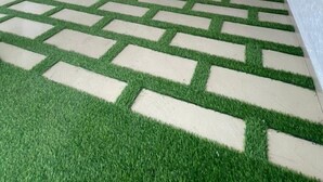 An indoor area with artificial grass flooring, a wooden ceiling with hanging foliage, and a glass door with informational signage. - Calawazobia hotel (Uyo)
