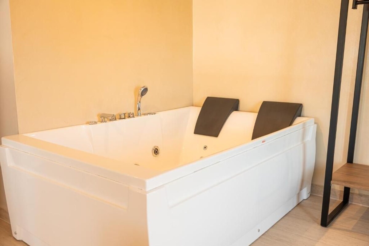 A modern bathroom with a large white bathtub, a shower, and a wooden bench.