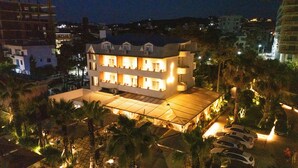 A multi-story hotel with a flat roof terrace, surrounded by palm trees and other vegetation. - Vila Lasko (Golem)