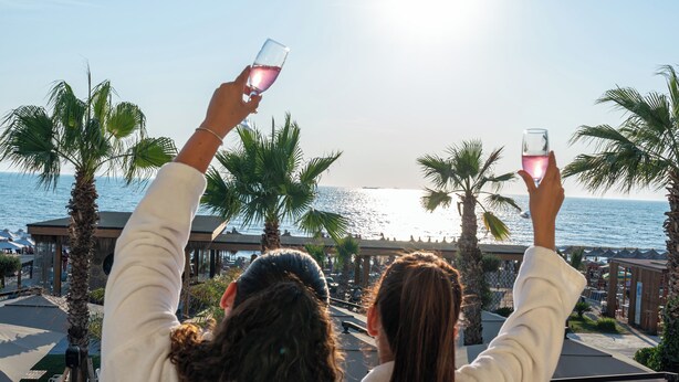Two people in white robes overlooking a beach with palm trees and a pool area. - Vila Lasko (Golem)