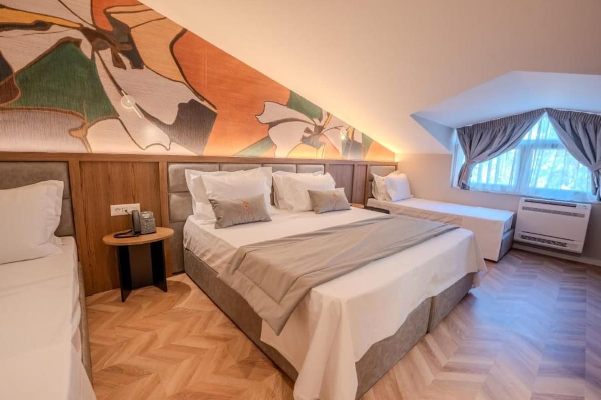 A hotel room with a large bed, a smaller bed, a nightstand, a wall-mounted telephone, and a window with curtains.