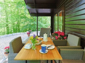 Una terrazza esterna con mobili in vimini, un tavolo di legno apparecchiato con teiera, tazze e fiori.