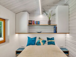 Una camera da letto con un letto, una mensola con libri e un vaso, e una finestra.