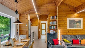 Een gezellig interieur van een chalet met een houten eethoek, een bank en een boekenplank.