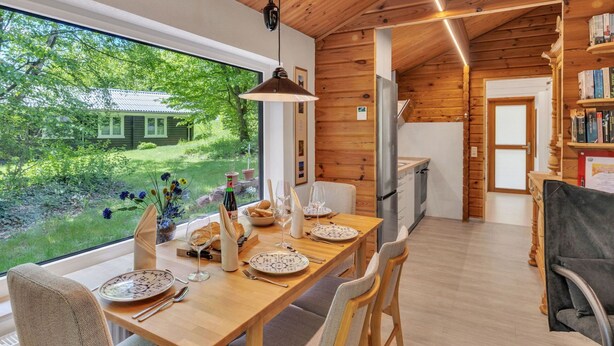 Een houten interieur met een eettafel gedekt voor twee personen, een keuken en uitzicht op een groen landschap.