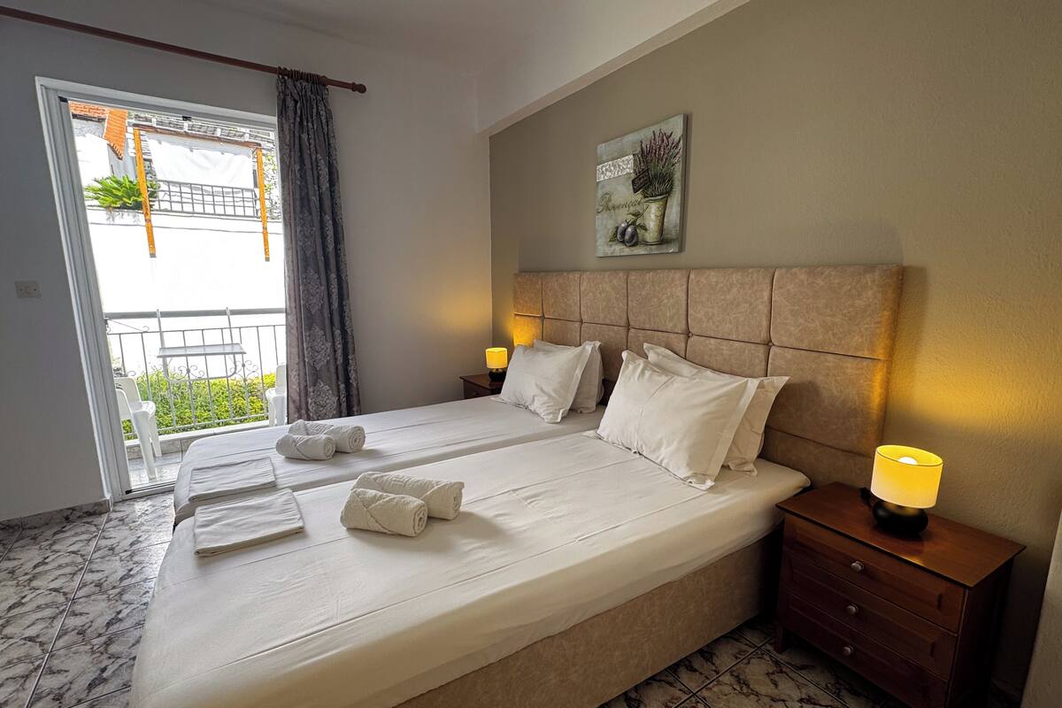 A hotel room with a large bed, two bedside tables with lamps, a balcony with a view, and a painting on the wall.