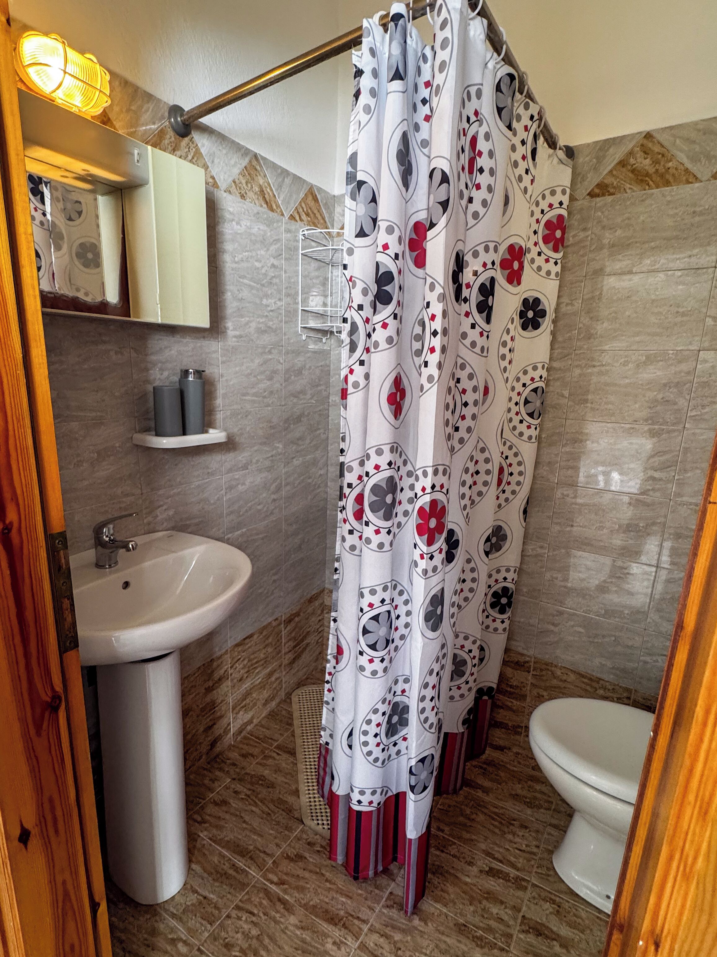 A bathroom with a white sink, a toilet, a shower curtain with a floral pattern, a mirror above the sink, and a towel rack.