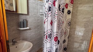 A bathroom with a white sink, a toilet, a shower curtain with a floral pattern, a mirror above the sink, and a towel rack. - Skiathos Platis House (Skiathos)
